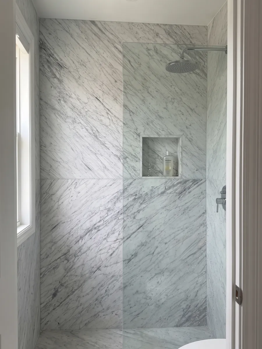Ducha revestida de mármol Carrara del piso al techo con un nicho de la misma piedra