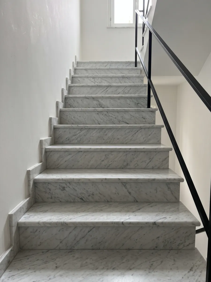 Escalera interior con peldaños de mármol blanco Carrara: blanco grisáceo con un dibujo gris fino y difuso repartido por toda la superficie