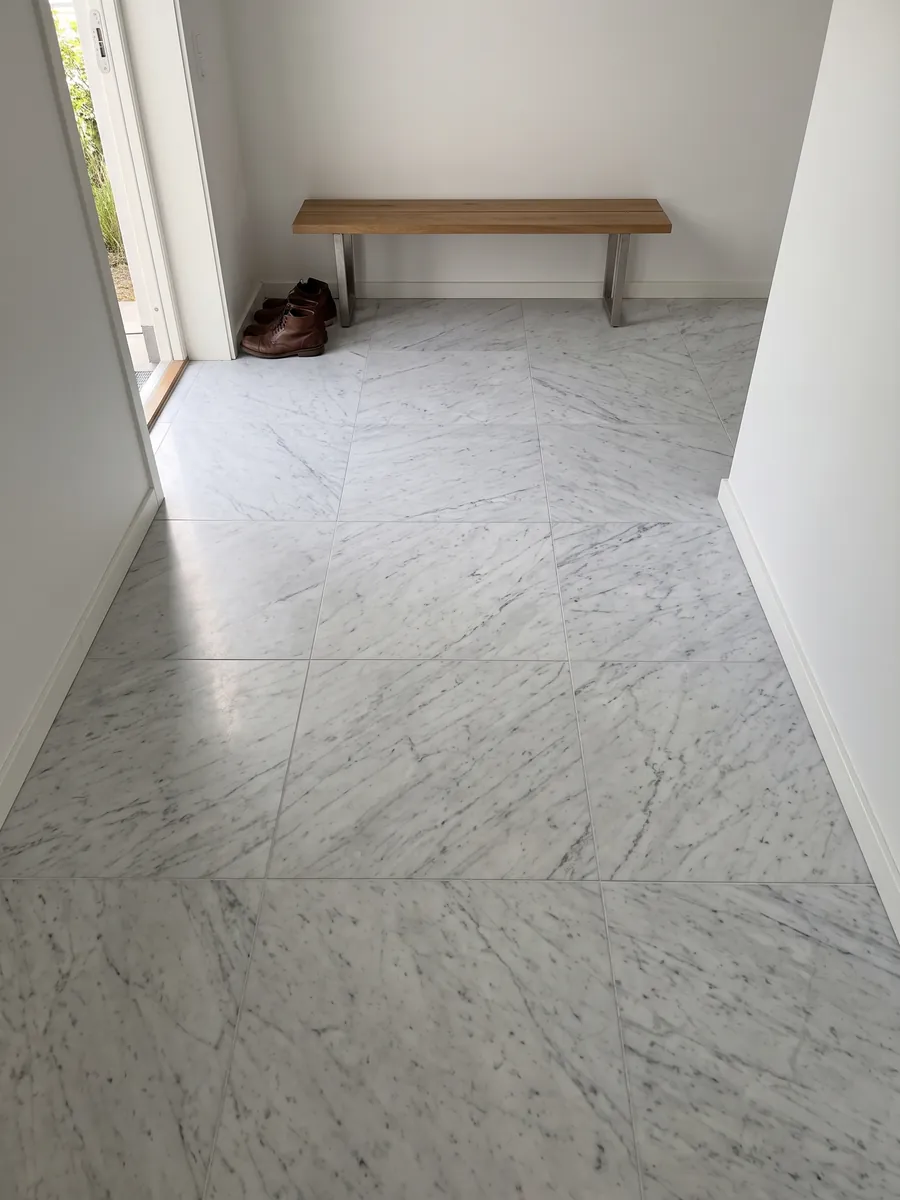Piso de recibidor en placas grandes de mármol blanco Carrara: blanco grisáceo con un dibujo gris fino y difuso repartido por toda la superficie