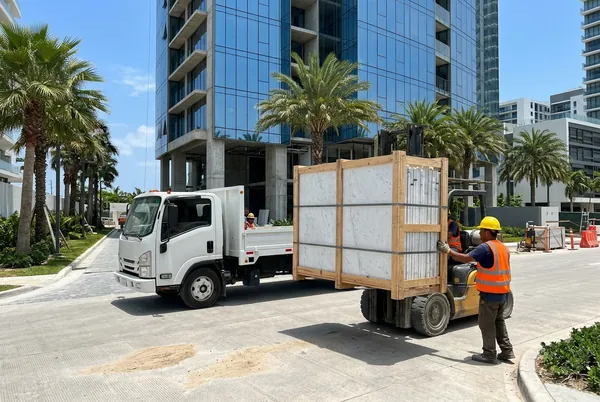 Montacargas descarga una caja de placas de mármol de un camión frente a una torre en construcción