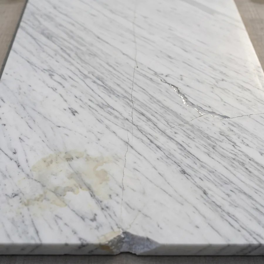 Placa de mármol Carrara de segunda selección con fisuras, una grieta rellena con resina, una mancha y una esquina dañada