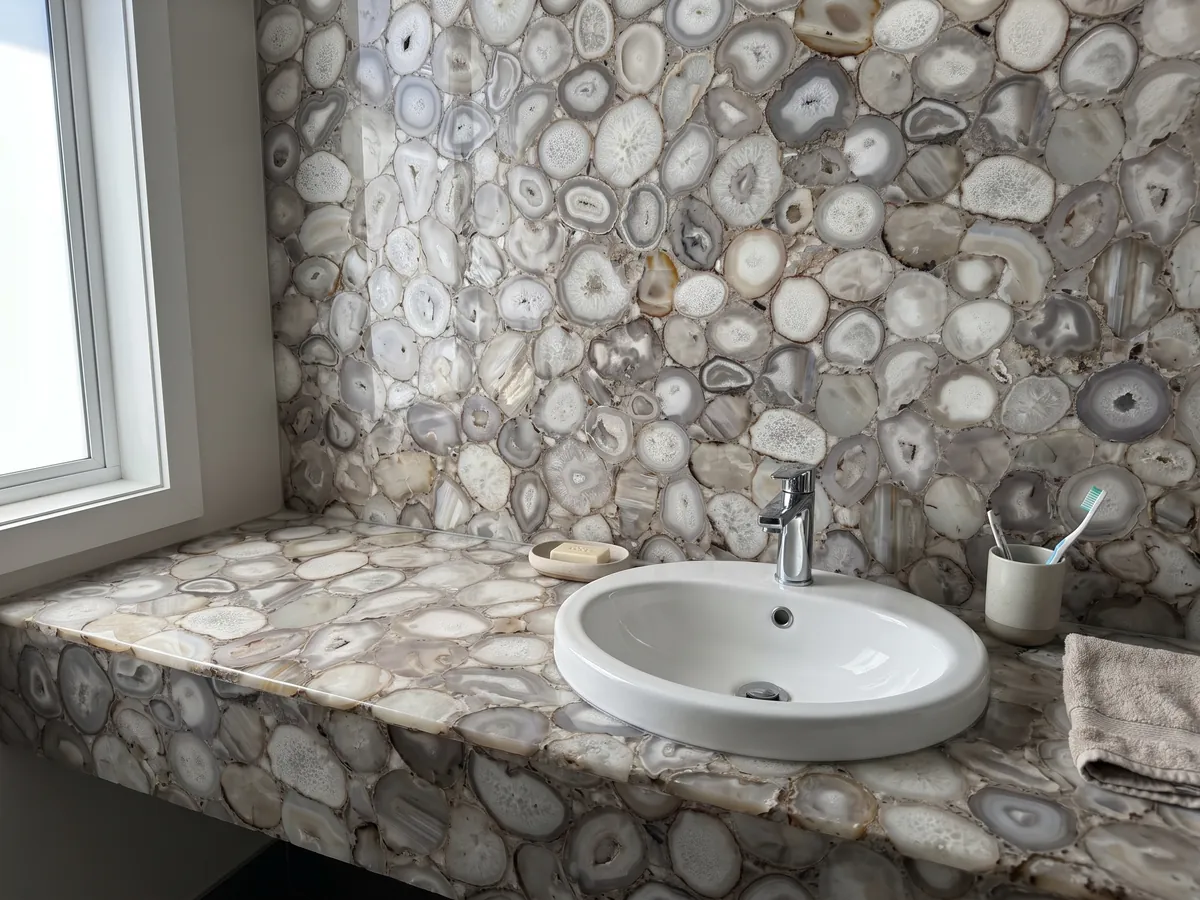 Cubierta de lavabo y pared de baño en Ágata Gris con lavamanos blanco y grifería cromada: rodajas de ágata gris beige y blanca, en tonos neutros