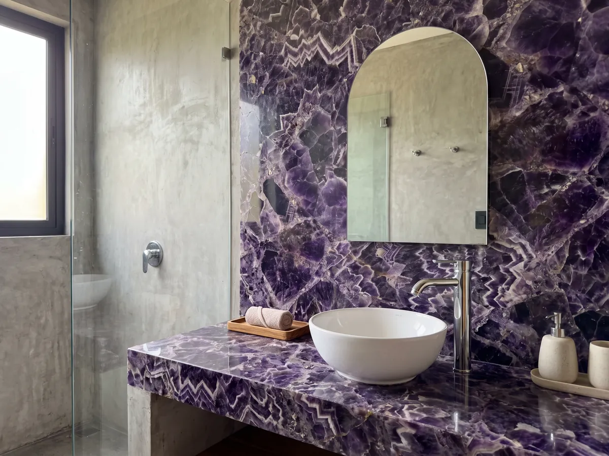 Cubierta de lavabo y pared de baño en Amatista con lavamanos blanco y grifería cromada: cristales violeta oscuro con franjas blancas y lilas en zigzag