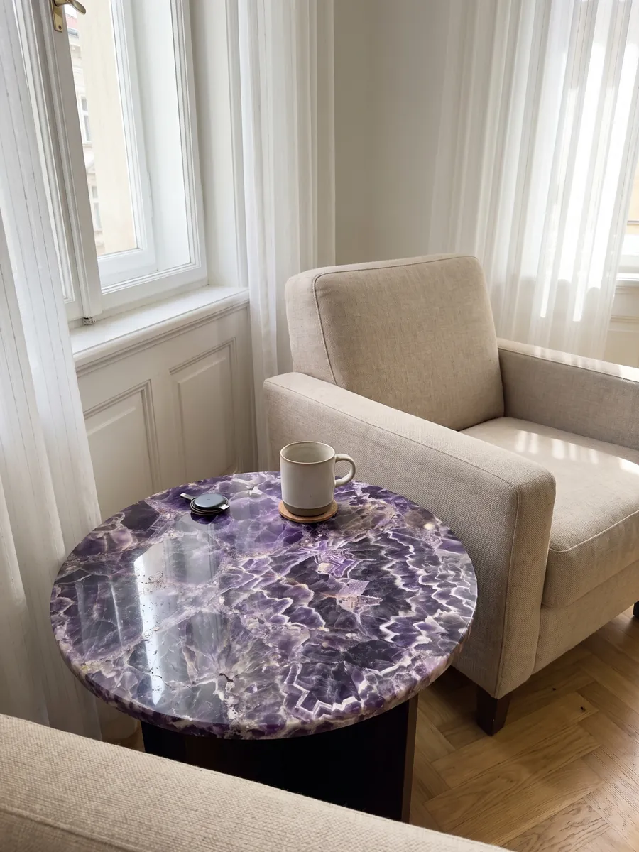 Mesa auxiliar con cubierta de Amatista junto a un sillón: cristales violeta oscuro con franjas blancas y lilas en zigzag