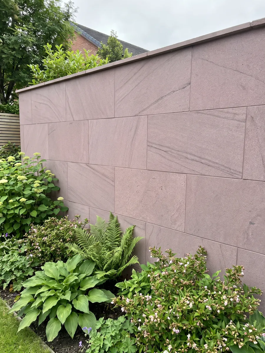 Muro de jardín revestido con Arenisca Santafiora Brown con plantas delante: superficie de grano fino color malva casi homogénea, sin vetas marcadas