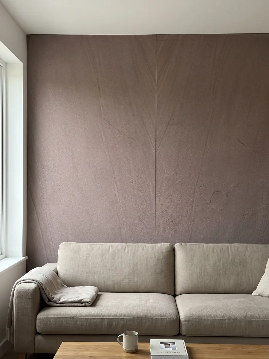 Pared de sala revestida con placas de Arenisca Santafiora Brown abiertas en libro detrás de un sofá: superficie de grano fino color malva casi homogénea, sin vetas marcadas