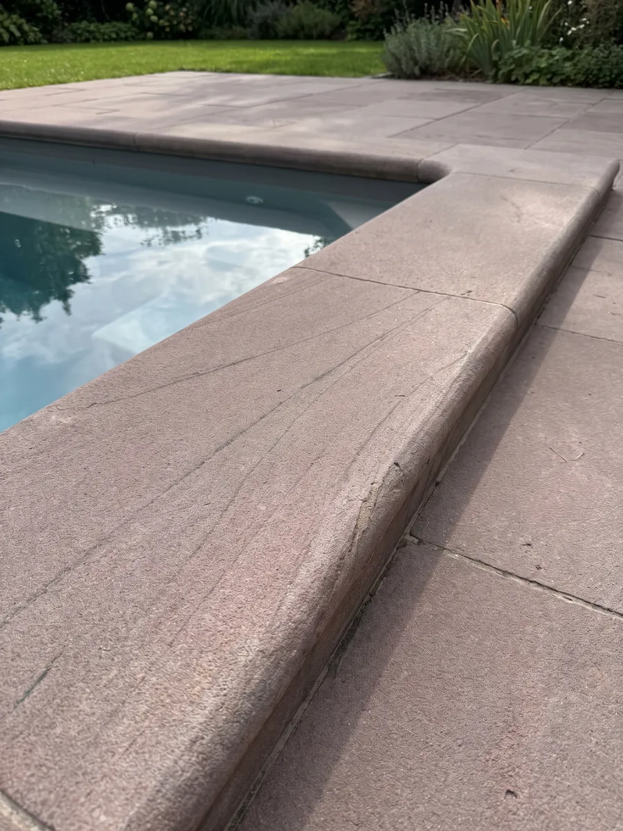 Borde y entorno de piscina en Arenisca Santafiora Brown en el jardín de una casa: superficie de grano fino color malva casi homogénea, sin vetas marcadas