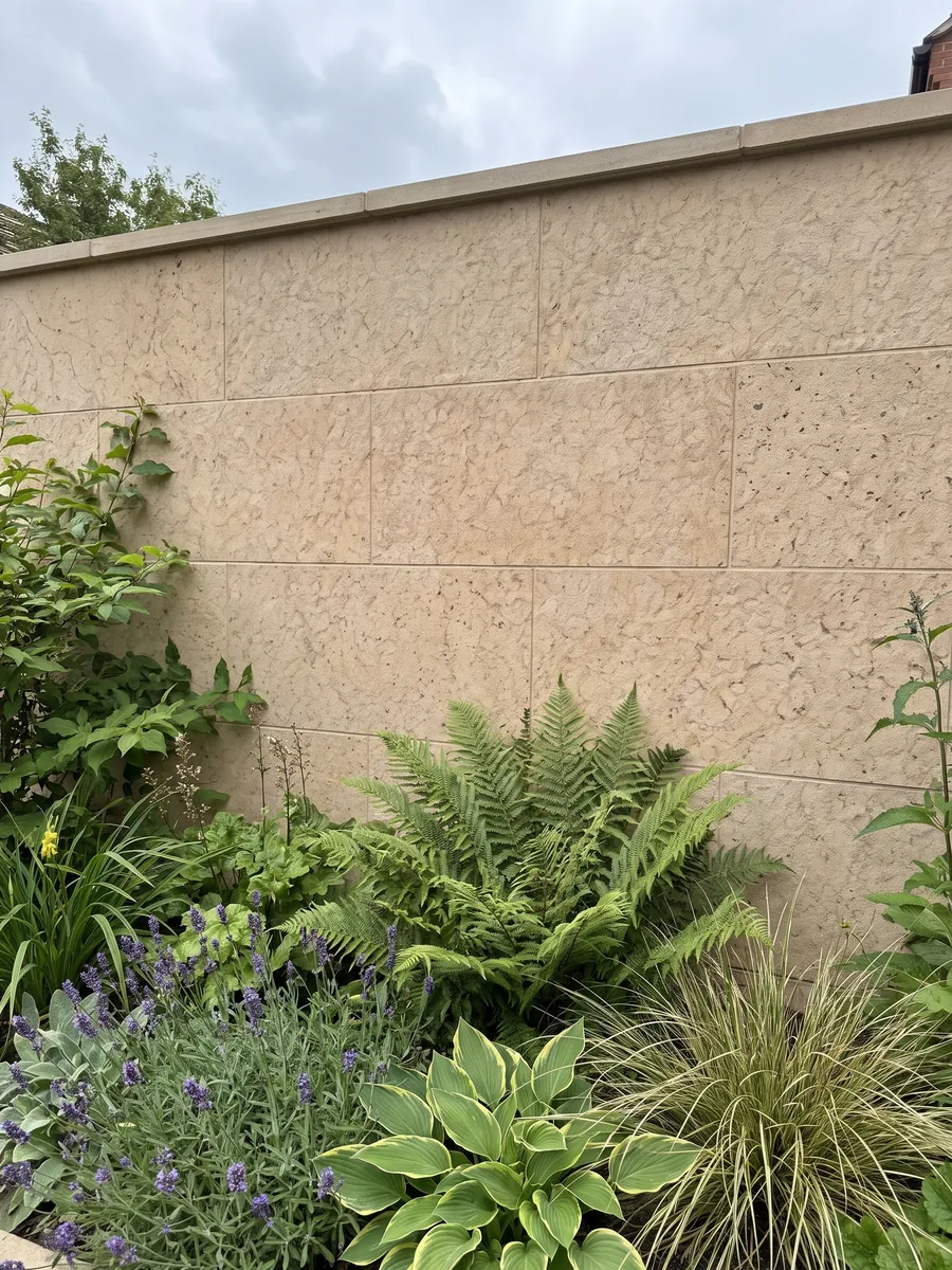 Muro de jardín revestido con Arenisca Santafiora Fiorita con plantas delante: beige arena con un dibujo de manchas en red, parecido a un craquelado fino