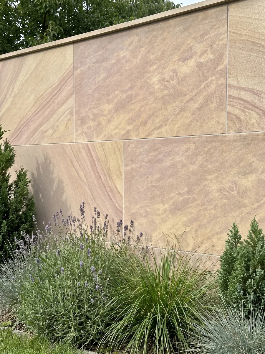 Muro de jardín revestido con Arenisca Santafiora Venata con plantas delante: beige arena con ondas diagonales suaves, como dunas de arena