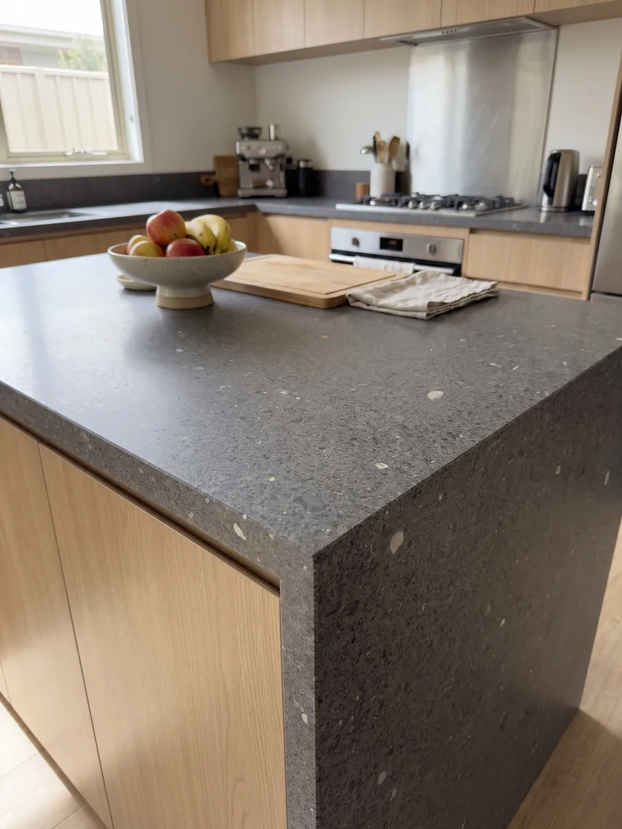 Isla de cocina con cubierta de Basalto Lavagrigia y canto recto en una cocina con luz natural: gris violáceo granulado tipo sal y pimienta con inclusiones blancas sueltas