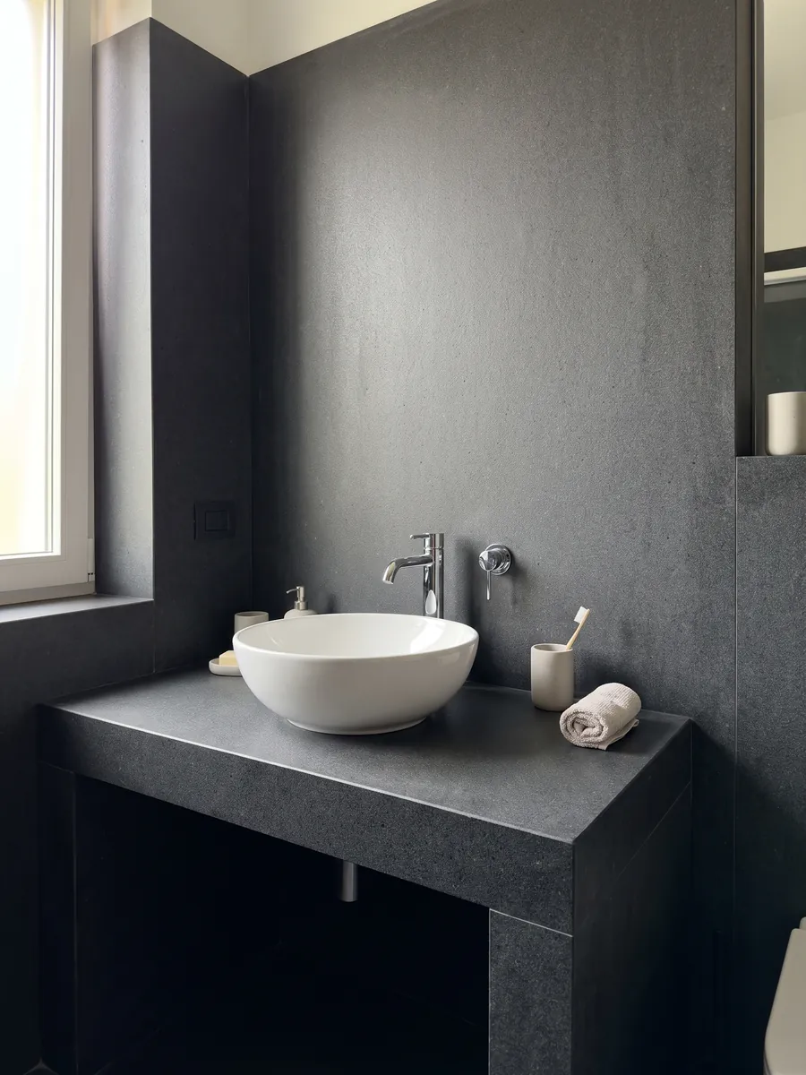 Cubierta de lavabo y pared de baño en Basalto Pietra Lavica con lavamanos blanco y grifería cromada: gris casi negro, homogéneo y de grano muy fino