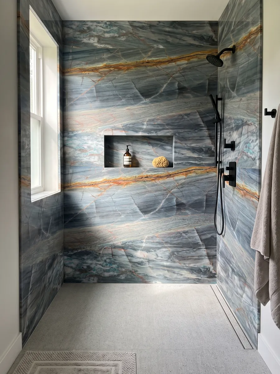 Ducha revestida con placas enteras de cuarcita azul Blue Atlantic con nicho empotrado: azul grisáceo en bandas horizontales con una veta naranja intensa arriba