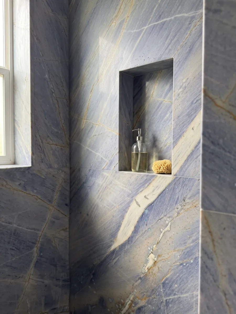 Ducha revestida con placas enteras de Cuarcita Azul Macaubas con nicho empotrado: fondo azul lavanda con una gran franja crema en diagonal y toques ocre
