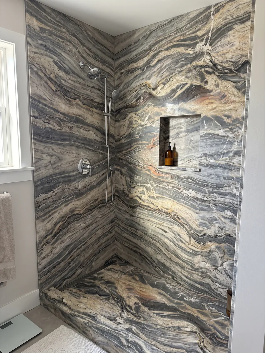 Ducha revestida con placas enteras de cuarcita beige Colorado con nicho empotrado: ondas horizontales crema y gris oscuro muy movidas, con algún toque naranja