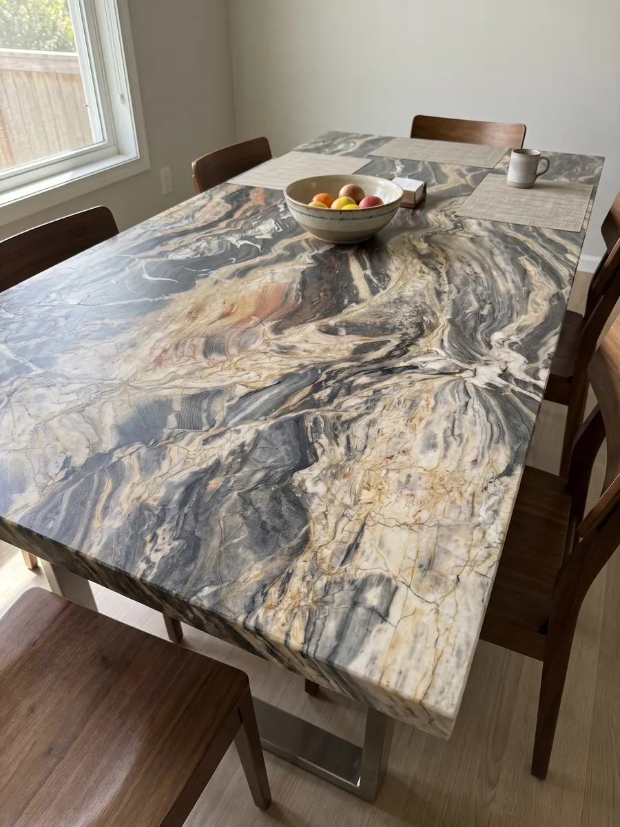 Mesa de comedor con cubierta de cuarcita beige Colorado sobre base de acero: ondas horizontales crema y gris oscuro muy movidas, con algún toque naranja