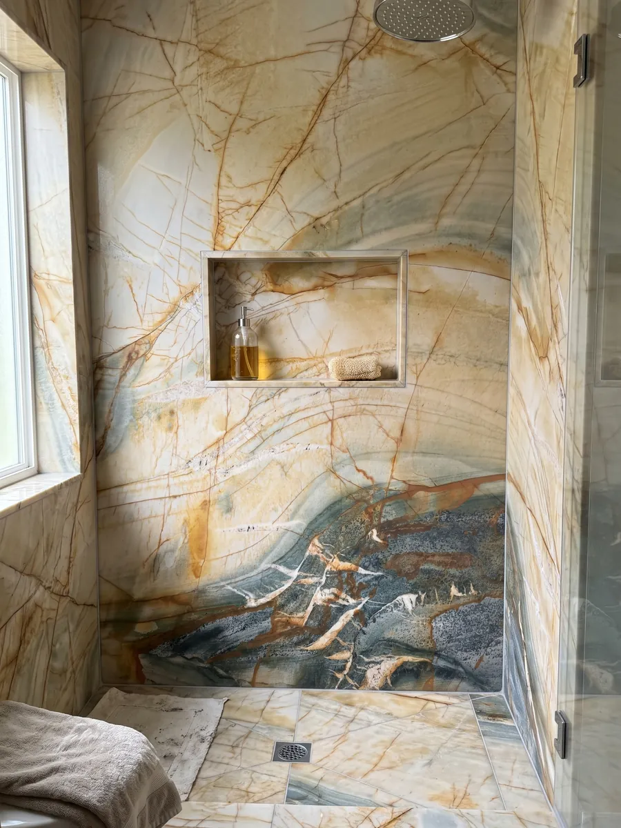 Ducha revestida con placas enteras de cuarcita beige Polaris Gold con nicho empotrado: crema y ocre con red de vetas naranja y zona gris petróleo inferior
