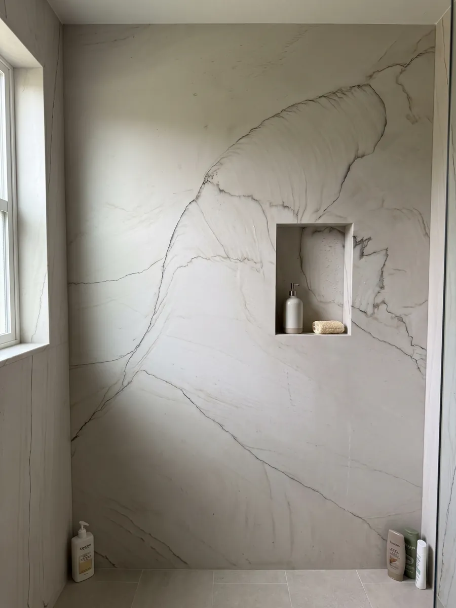 Ducha revestida con placas enteras de cuarcita blanca Dune con nicho empotrado: blanco hueso con una línea oscura fina que traza una gran curva