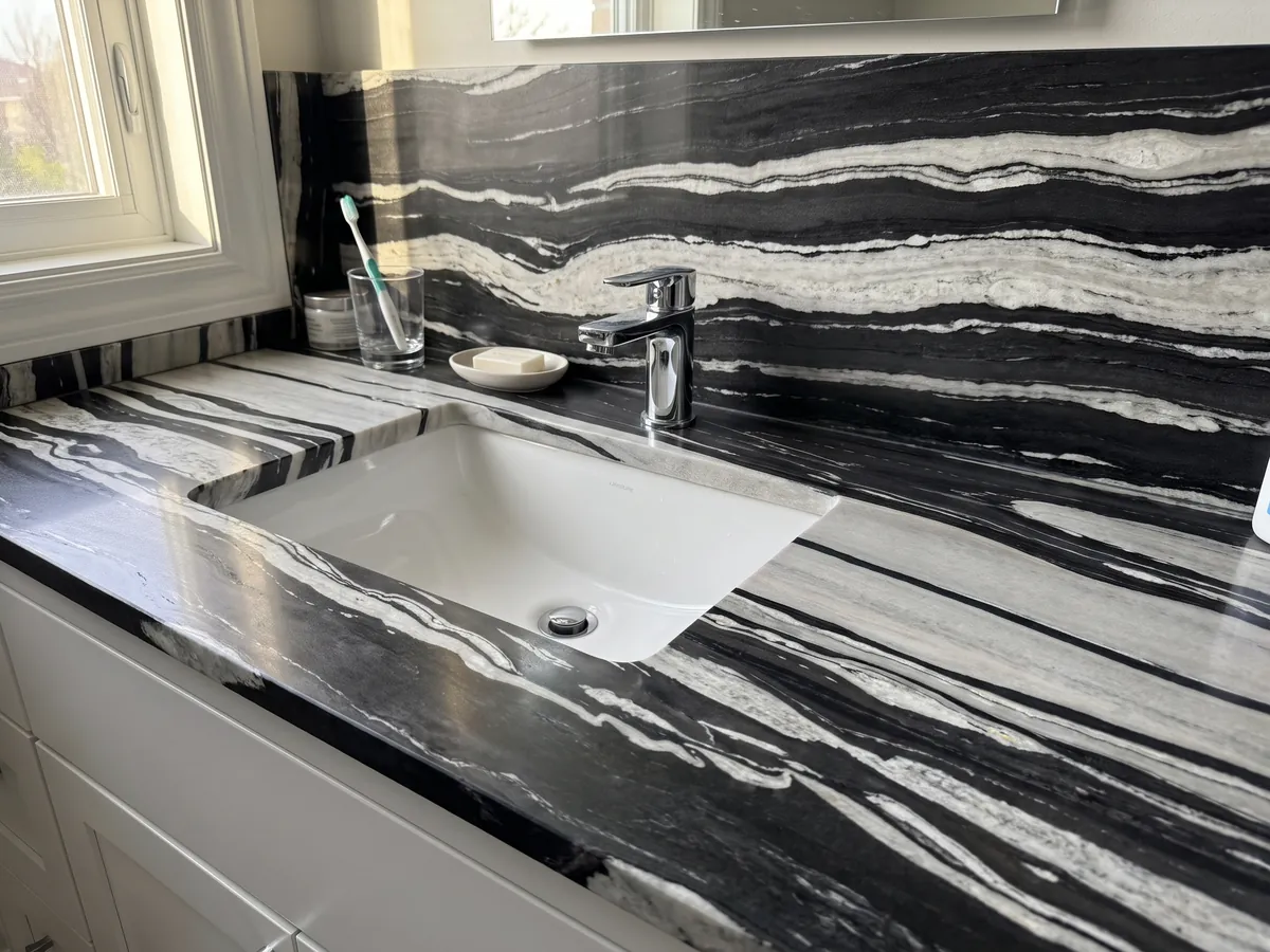 Cubierta de lavabo y pared de baño en cuarcita blanca White Copacabana con lavamanos blanco y grifería cromada: bandas horizontales blancas y negras alternadas de gran contraste