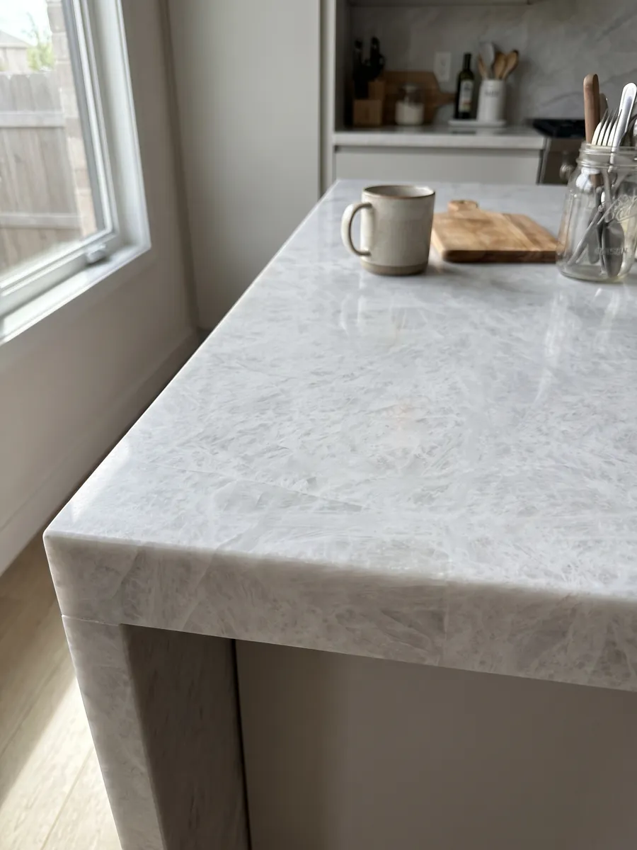Canto recto de una cubierta de cocina en cuarcita gris Cristallo con la veta continuando por el borde: blanco grisáceo casi uniforme con aspecto cristalino suave