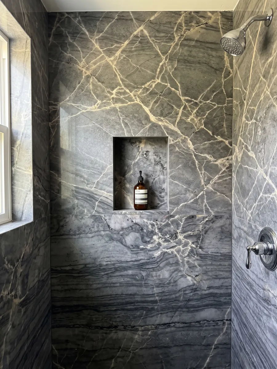 Ducha revestida con placas enteras de cuarcita gris London Grey con nicho empotrado: gris carbón con red de vetas crema y ondas horizontales oscuras