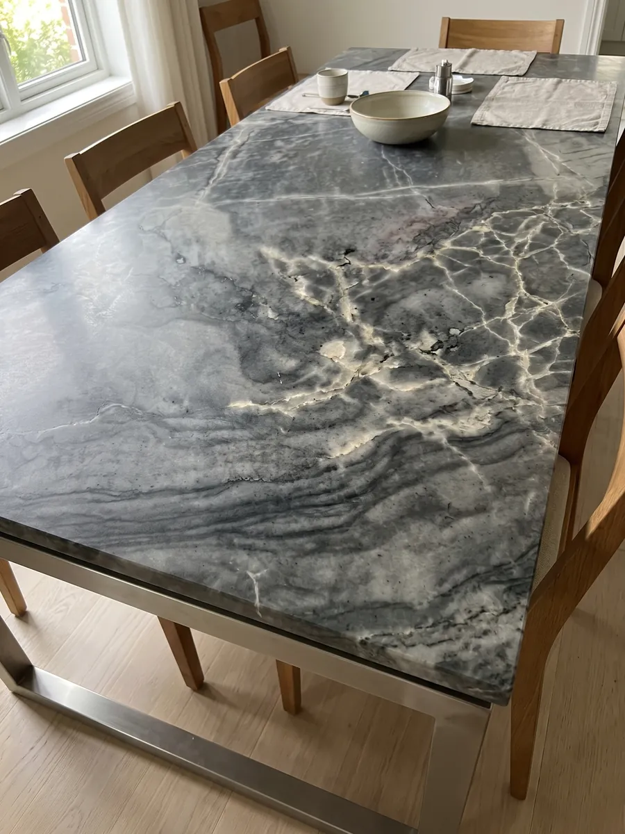 Mesa de comedor con cubierta de cuarcita gris London Grey sobre base de acero: gris carbón con red de vetas crema y ondas horizontales oscuras