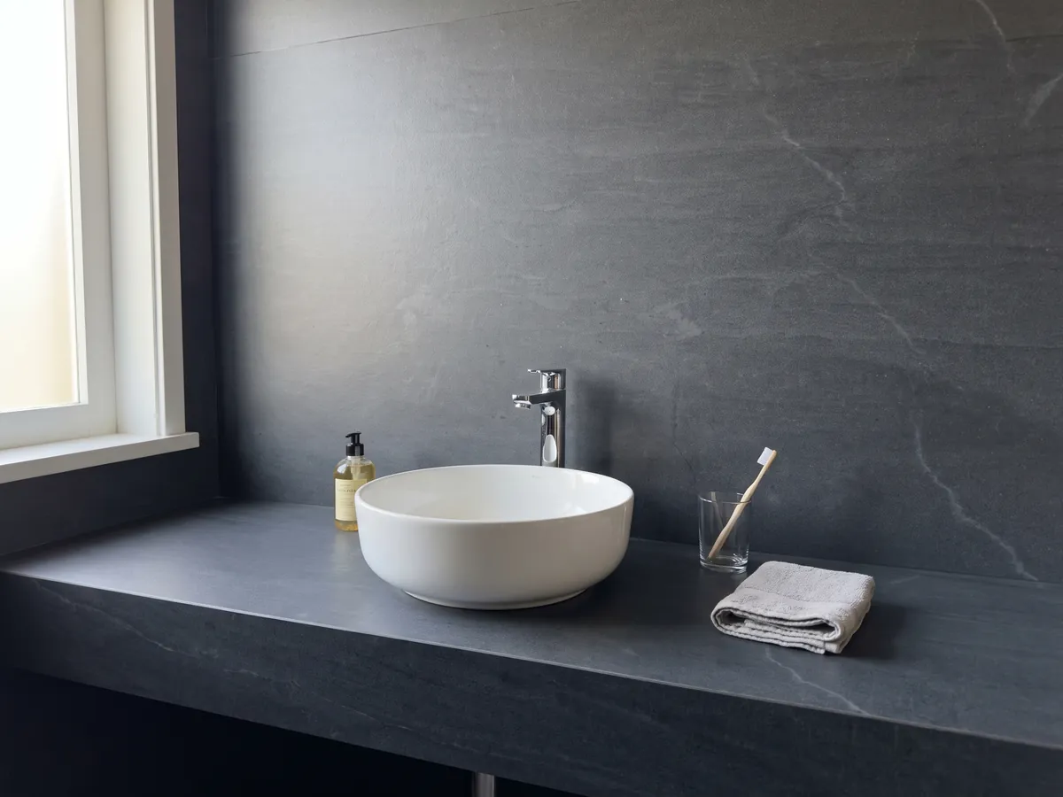 Cubierta de lavabo y pared de baño en cuarcita gris Pietra del Cardoso con lavamanos blanco y grifería cromada: gris pizarra oscuro uniforme, sin dibujo