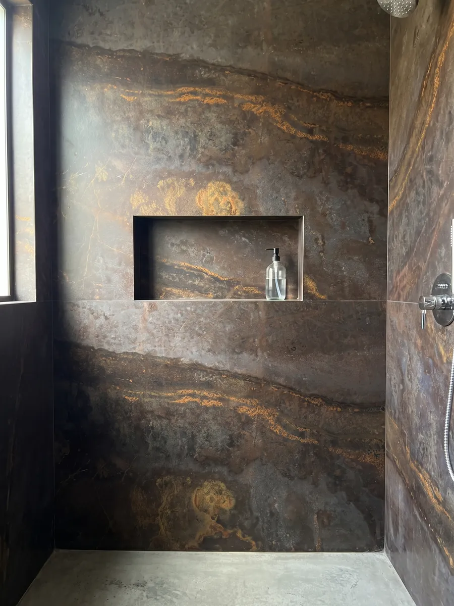 Ducha revestida con placas enteras de cuarcita marrón Bronzite con nicho empotrado: marrón oscuro con una franja horizontal salpicada de destellos naranja dorado
