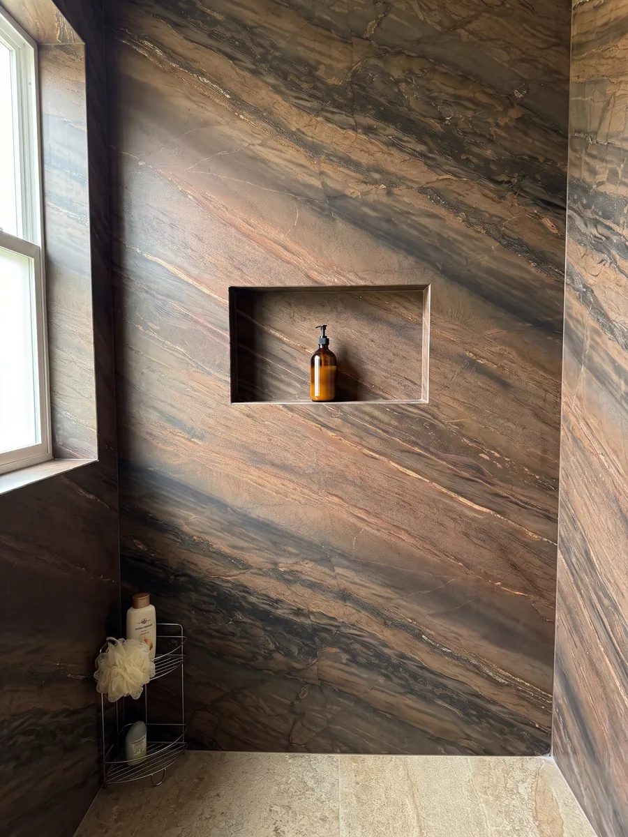 Ducha revestida con placas enteras de cuarcita marrón Elegant Brown con nicho empotrado: marrón cobrizo en bandas diagonales paralelas con líneas doradas finas