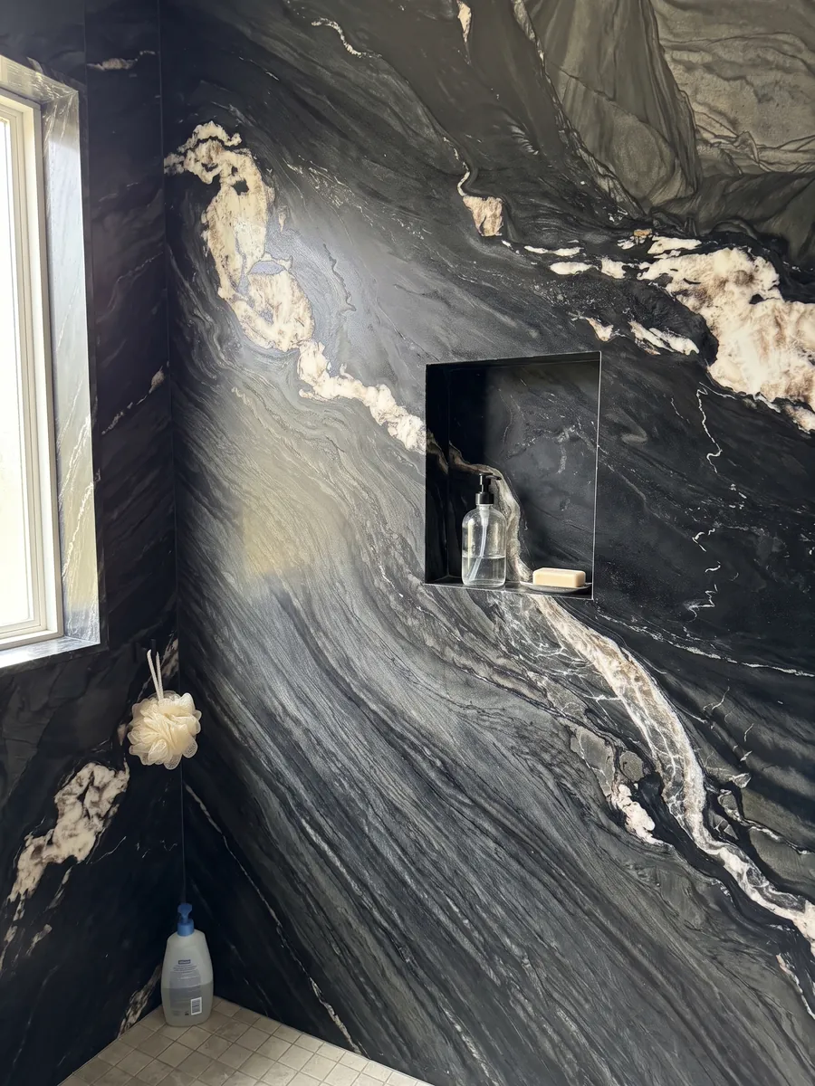 Ducha revestida con placas enteras de cuarcita negra Black Tempest con nicho empotrado: negro con ondas grises y una línea de grandes manchas blancas en diagonal