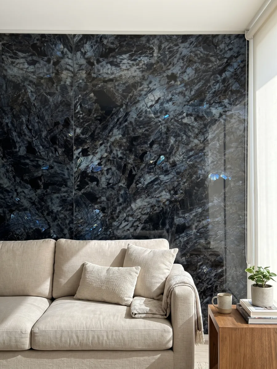 Pared de sala revestida con placas de cuarcita negra Lemurian abiertas en libro detrás de un sofá: negro de cristales grandes con destellos azul iridiscente