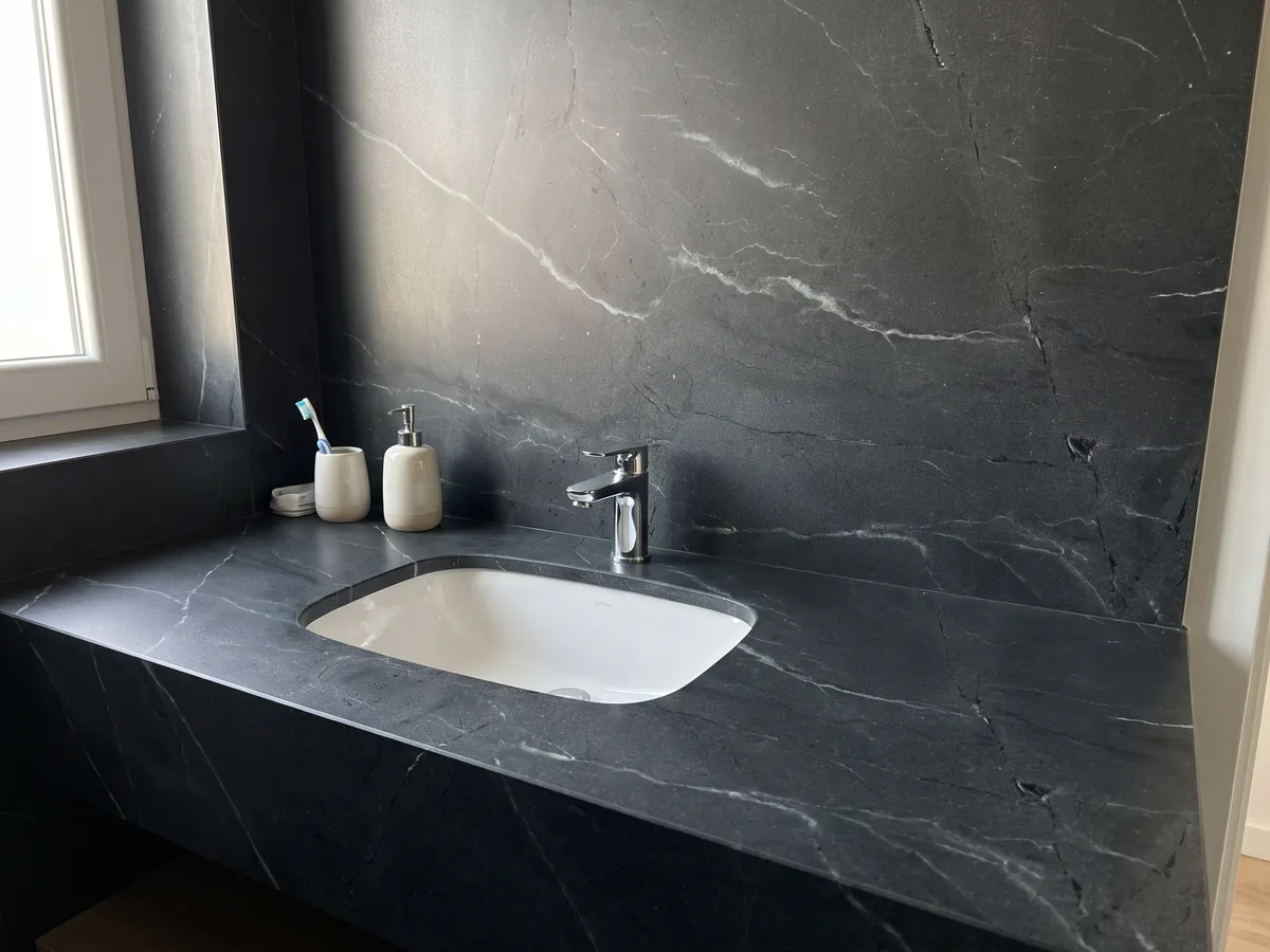 Cubierta de lavabo y pared de baño en cuarcita negra Negresco con lavamanos blanco y grifería cromada: negro con vetas blancas finas y escasas en diagonal