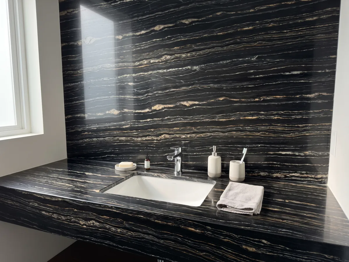 Cubierta de lavabo y pared de baño en cuarcita negra Tropical Storm con lavamanos blanco y grifería cromada: negro con finas líneas horizontales blancas y doradas