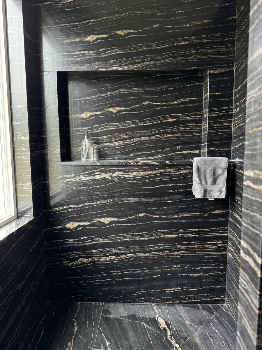 Ducha revestida con placas enteras de cuarcita negra Tropical Storm con nicho empotrado: negro con finas líneas horizontales blancas y doradas