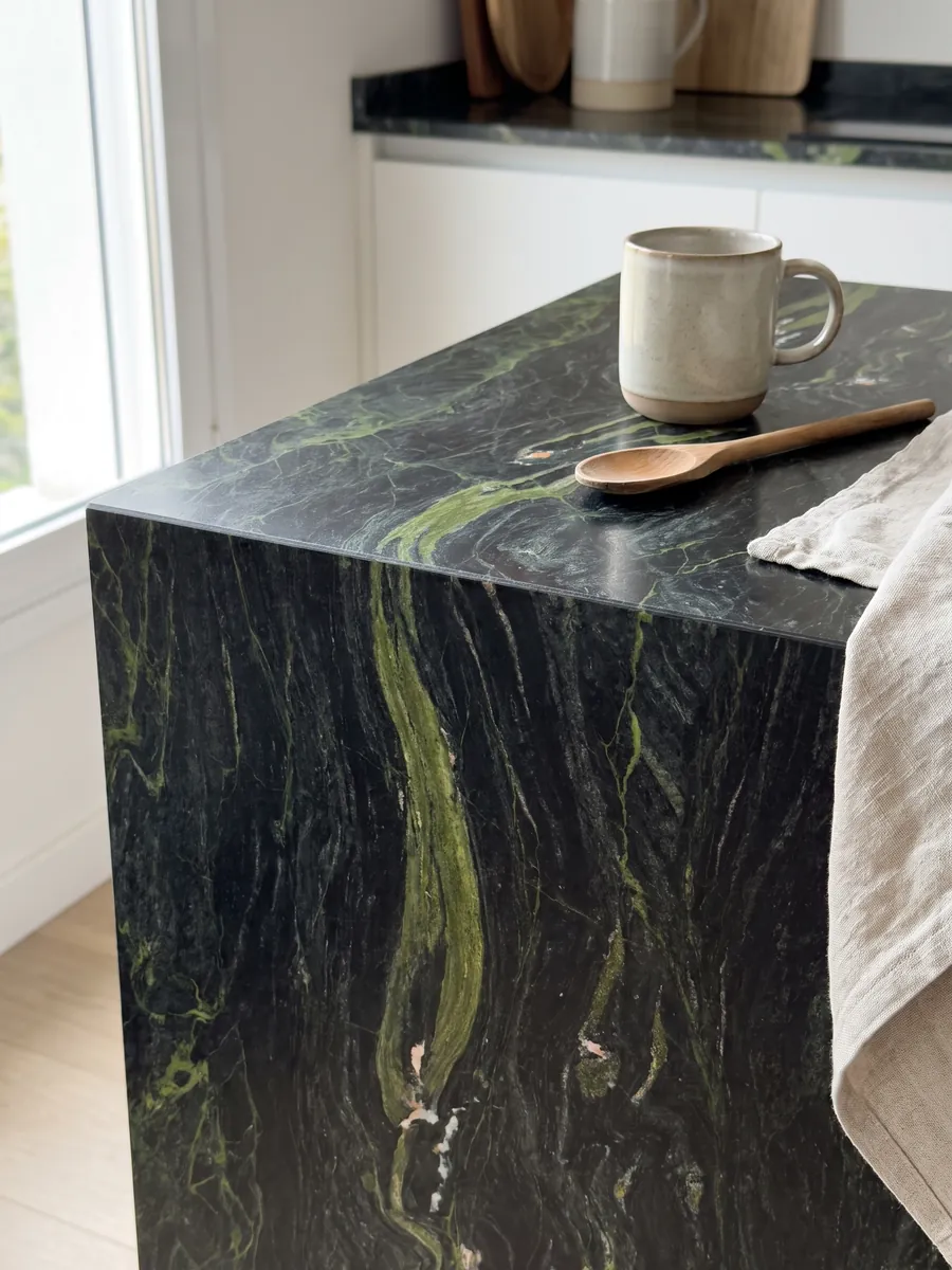 Canto recto de una cubierta de cocina en cuarcita negra Vancouver con la veta continuando por el borde: negro verdoso con ondas verde lima horizontales