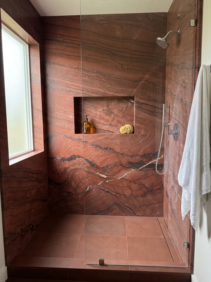 Ducha revestida con placas enteras de cuarcita roja Fusion Red con nicho empotrado: rojo ladrillo con ondas oscuras horizontales y una fina veta blanca
