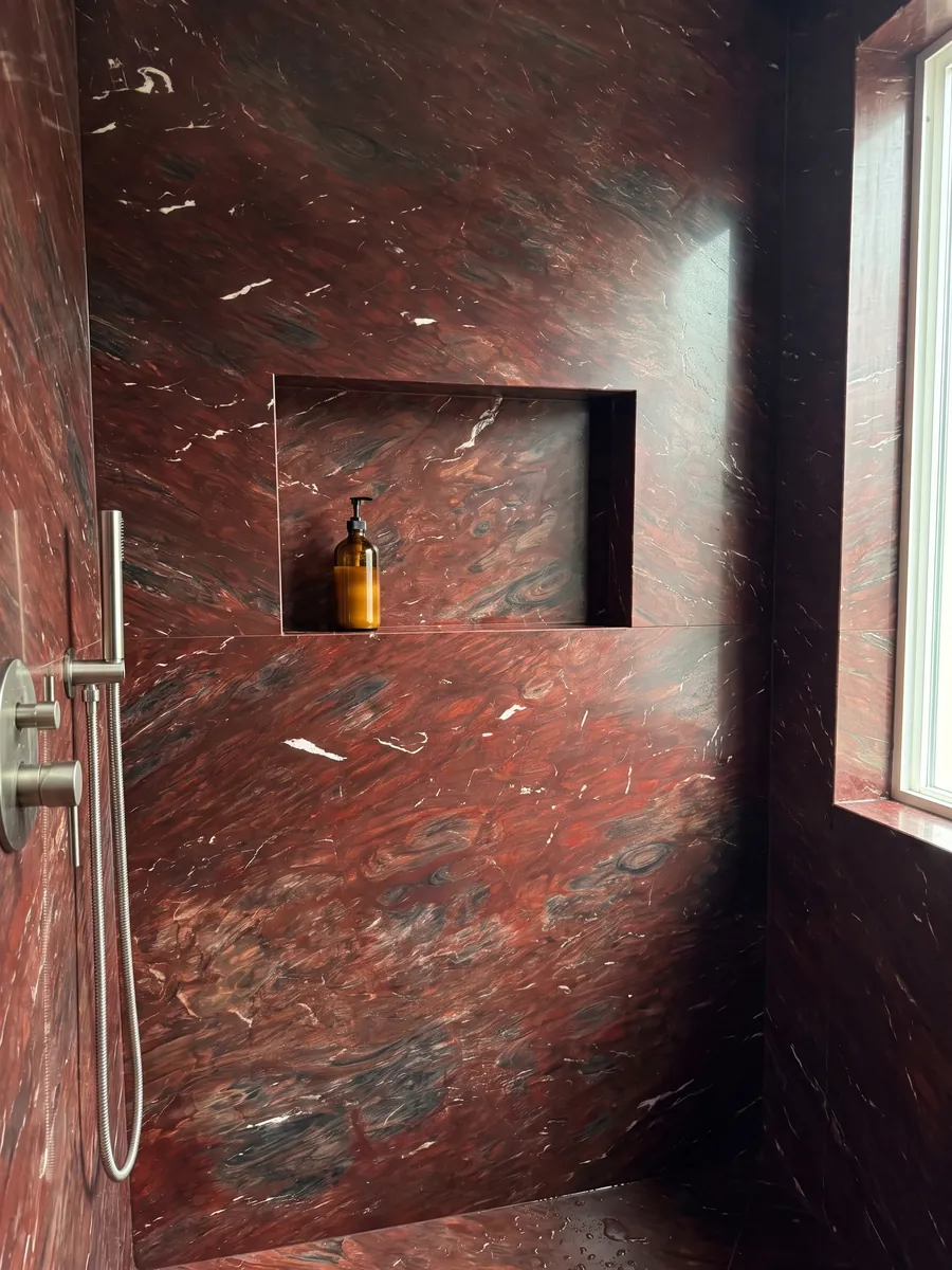 Ducha revestida con placas enteras de cuarcita roja Napoleon Bordeaux con nicho empotrado: rojo vino intenso con zonas oscuras y trazos blancos pequeños