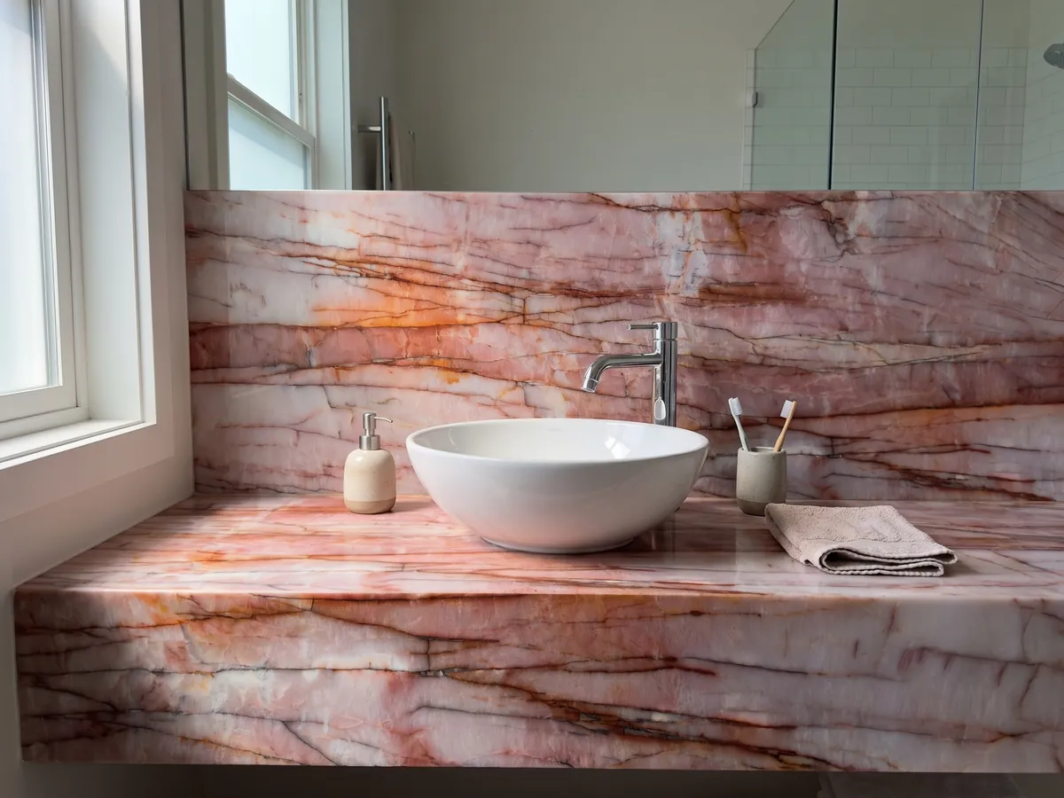 Cubierta de lavabo y pared de baño en cuarcita rosa Juliet con lavamanos blanco y grifería cromada: rosa intenso y blanco con vetas horizontales rojo óxido
