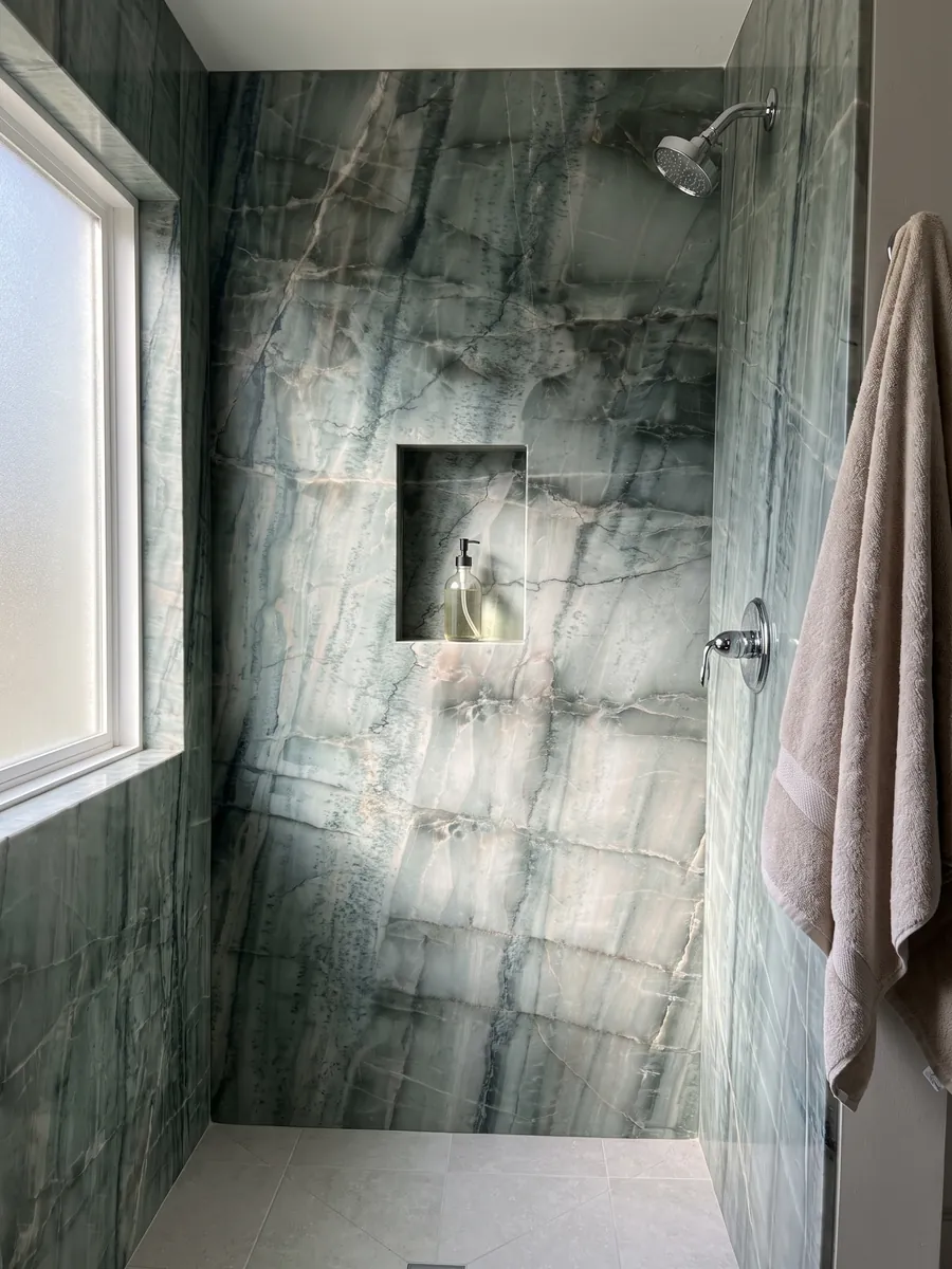 Ducha revestida con placas enteras de cuarcita verde da Vinci con nicho empotrado: verde grisáceo con cuadrícula de vetas oscuras verticales y bandas claras