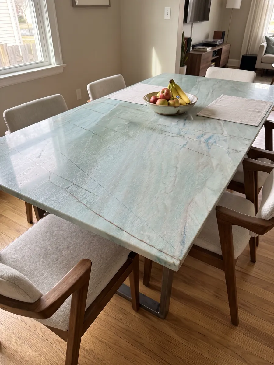 Mesa de comedor con cubierta de cuarcita verde Emerald Green sobre base de acero: verde agua claro con finas líneas oscuras verticales y pequeños destellos azules