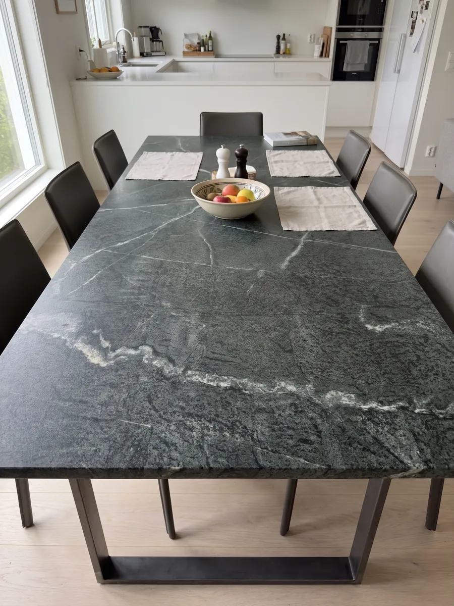 Mesa de comedor con cubierta de cuarcita verde Pietra Ollare sobre base de acero: verde casi negro granulado con una veta blanca serpenteante