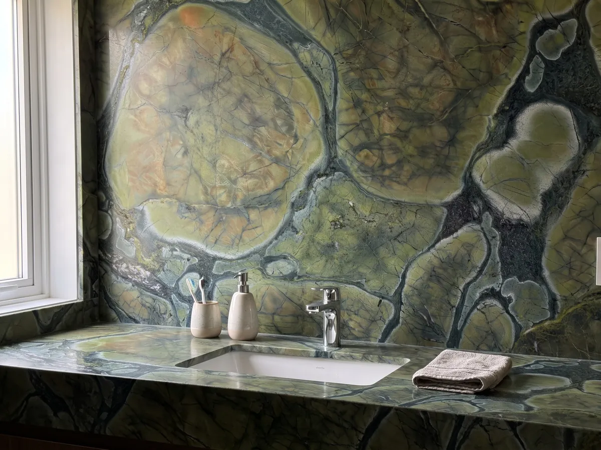 Cubierta de lavabo y pared de baño en cuarcita verde Victoria Regia con lavamanos blanco y grifería cromada: celdas redondeadas verde oliva con bordes oscuros, como hojas de nenúfar