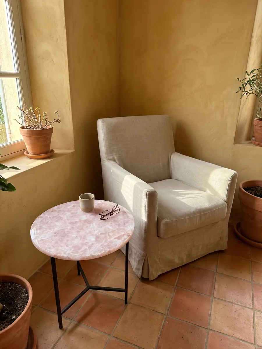Mesa auxiliar con cubierta de Cuarzo Rosa junto a un sillón: rosa pálido cristalino con fragmentos más blancos