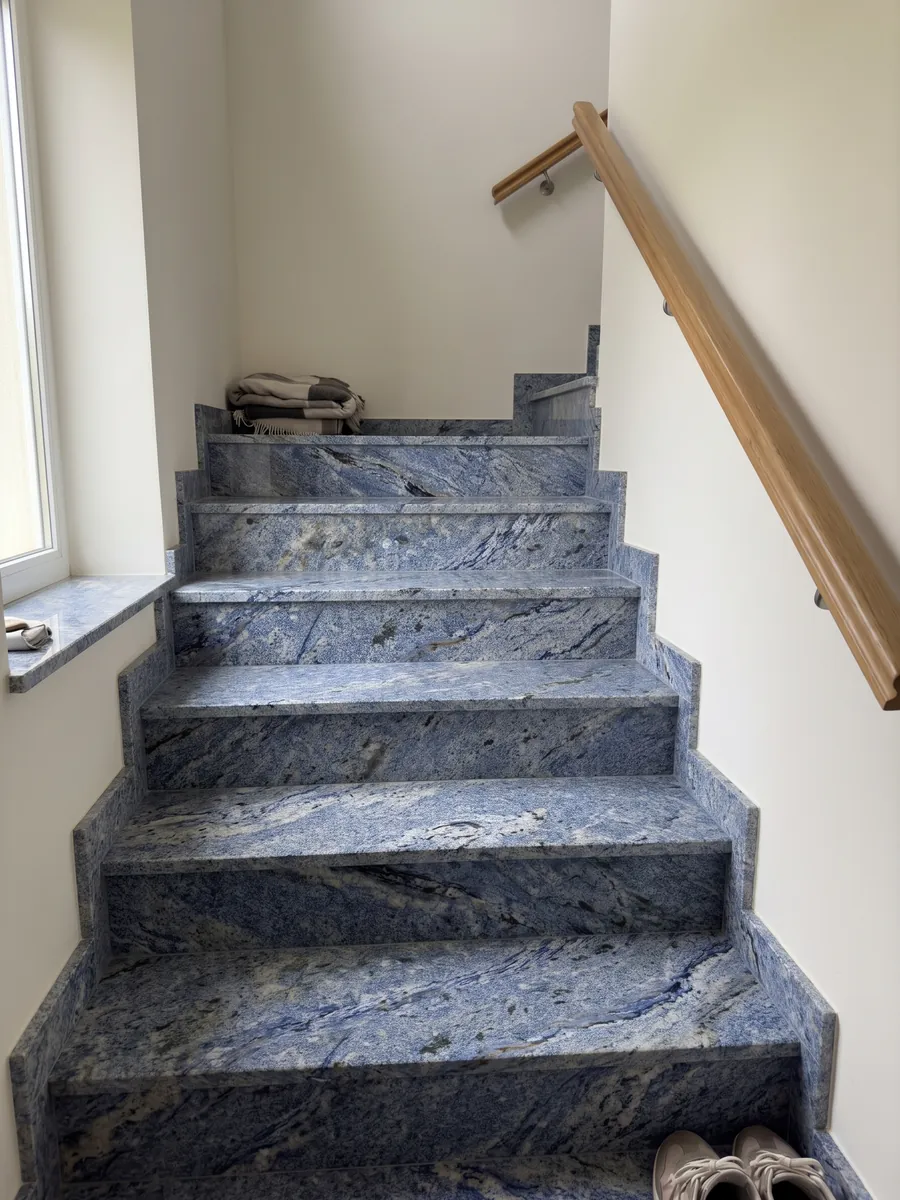 Escalera interior con peldaños de Granito Azul Bahia con pasamanos: azul intenso granulado con zonas blancas y manchas oscuras