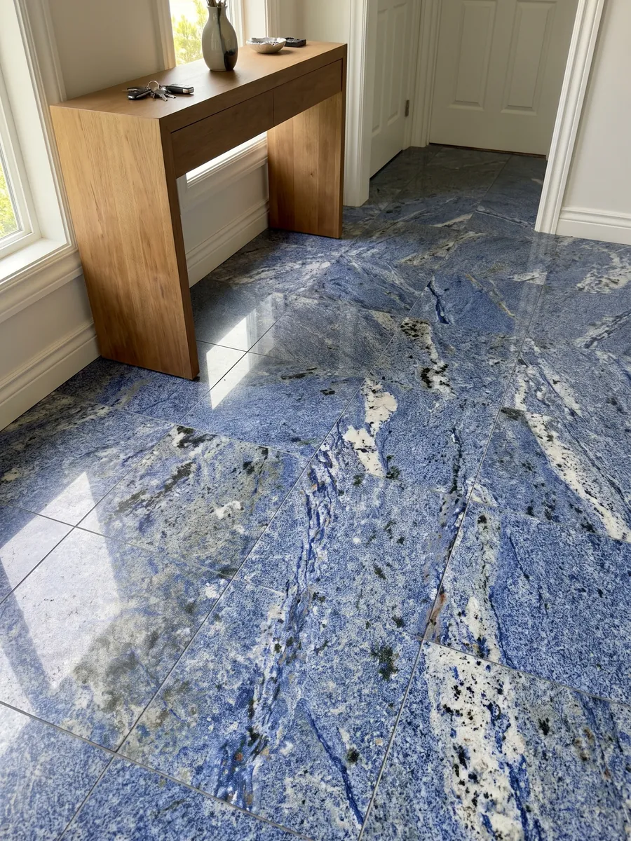 Piso de recibidor en placas grandes de Granito Azul Bahia con luz natural: azul intenso granulado con zonas blancas y manchas oscuras