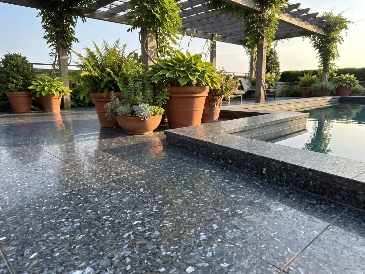 Piso de terraza y borde de piscina en granito azul Blue Pearl con macetas: gris azulado casi negro con cristales que brillan azul plateado