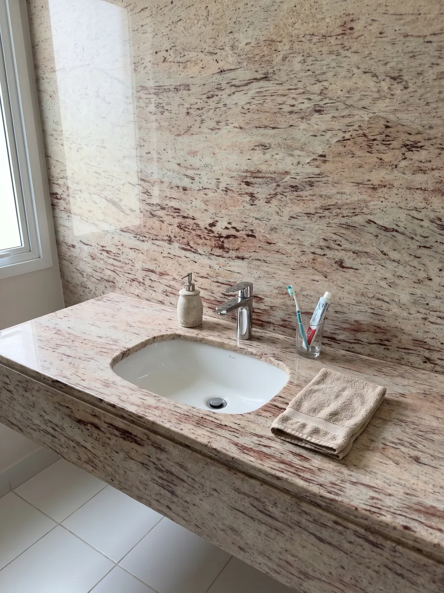 Cubierta de lavabo y pared de baño en granito beige Ivory Brown con lavamanos blanco y grifería cromada: marfil con trazos horizontales rojizos y burdeos