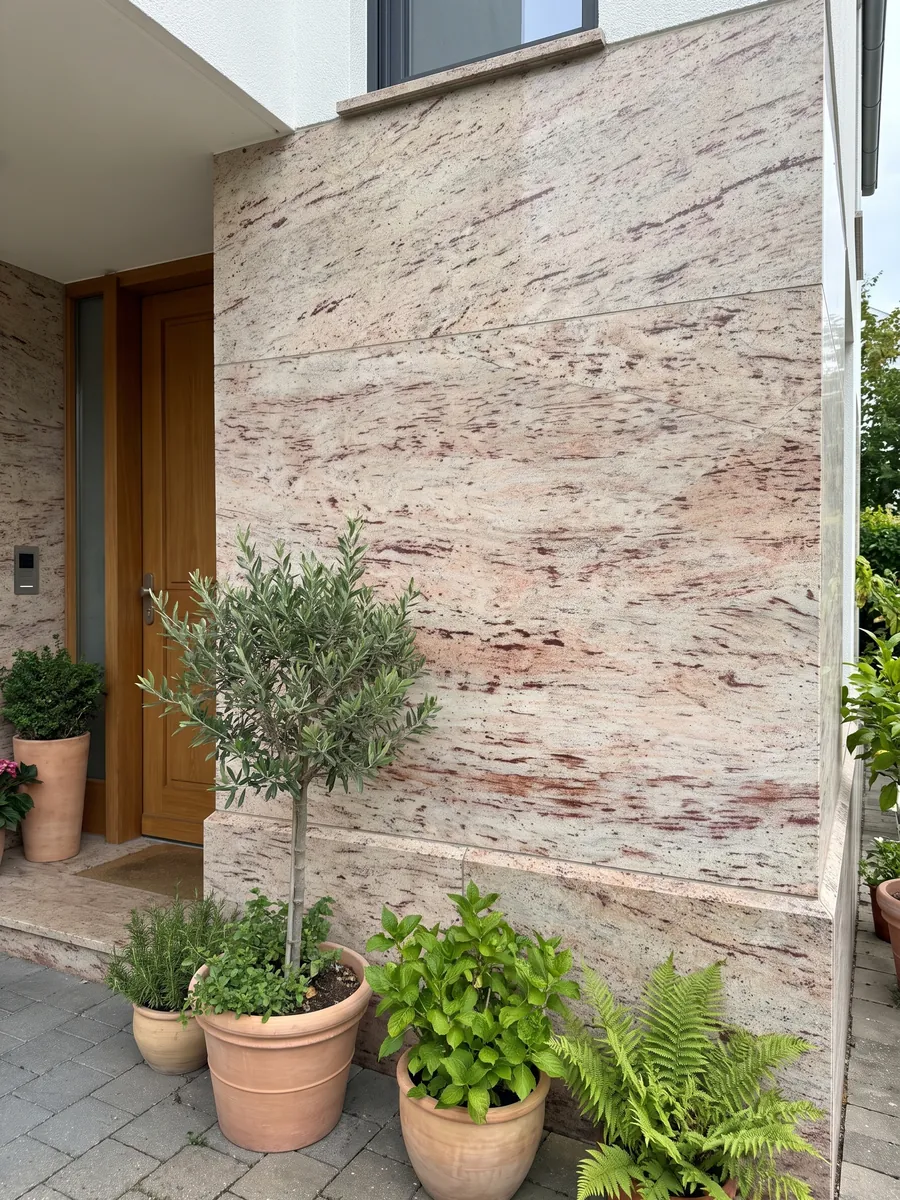 Fachada de casa revestida con granito beige Ivory Brown junto a una puerta de madera: marfil con trazos horizontales rojizos y burdeos