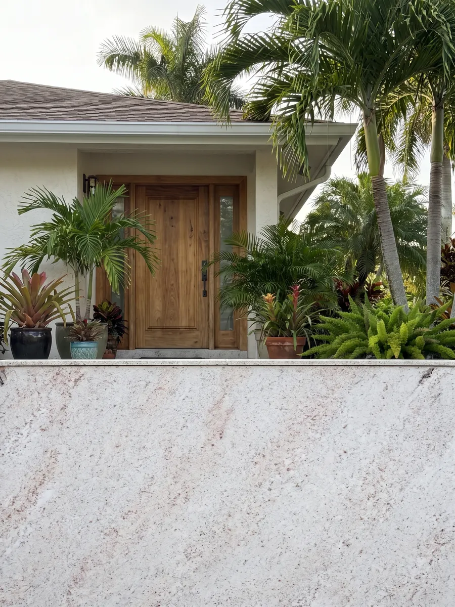 Fachada de casa revestida con granito blanco Branco Siena junto a una puerta de madera: blanco con un moteado fino rosado y gris