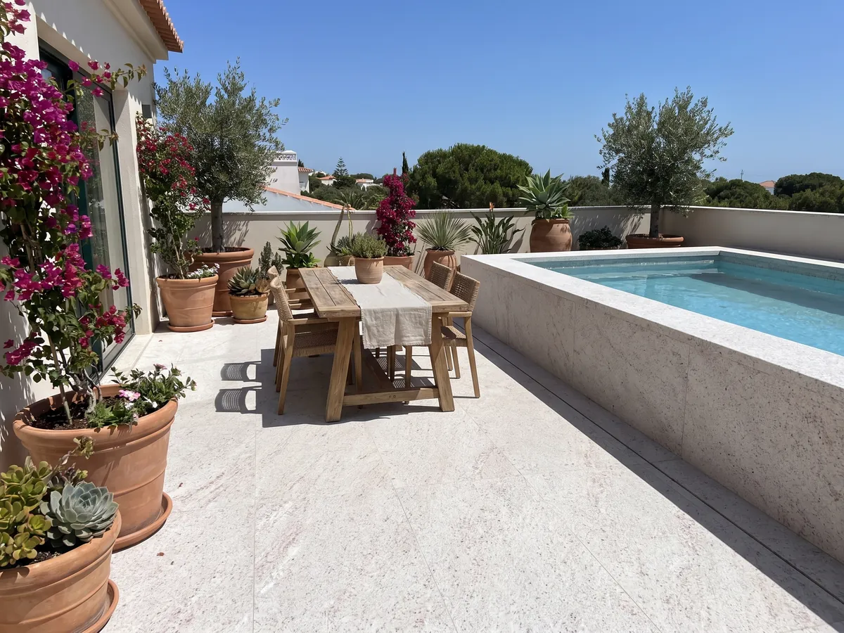 Piso de terraza y borde de piscina en granito blanco Branco Siena con macetas: blanco con un moteado fino rosado y gris