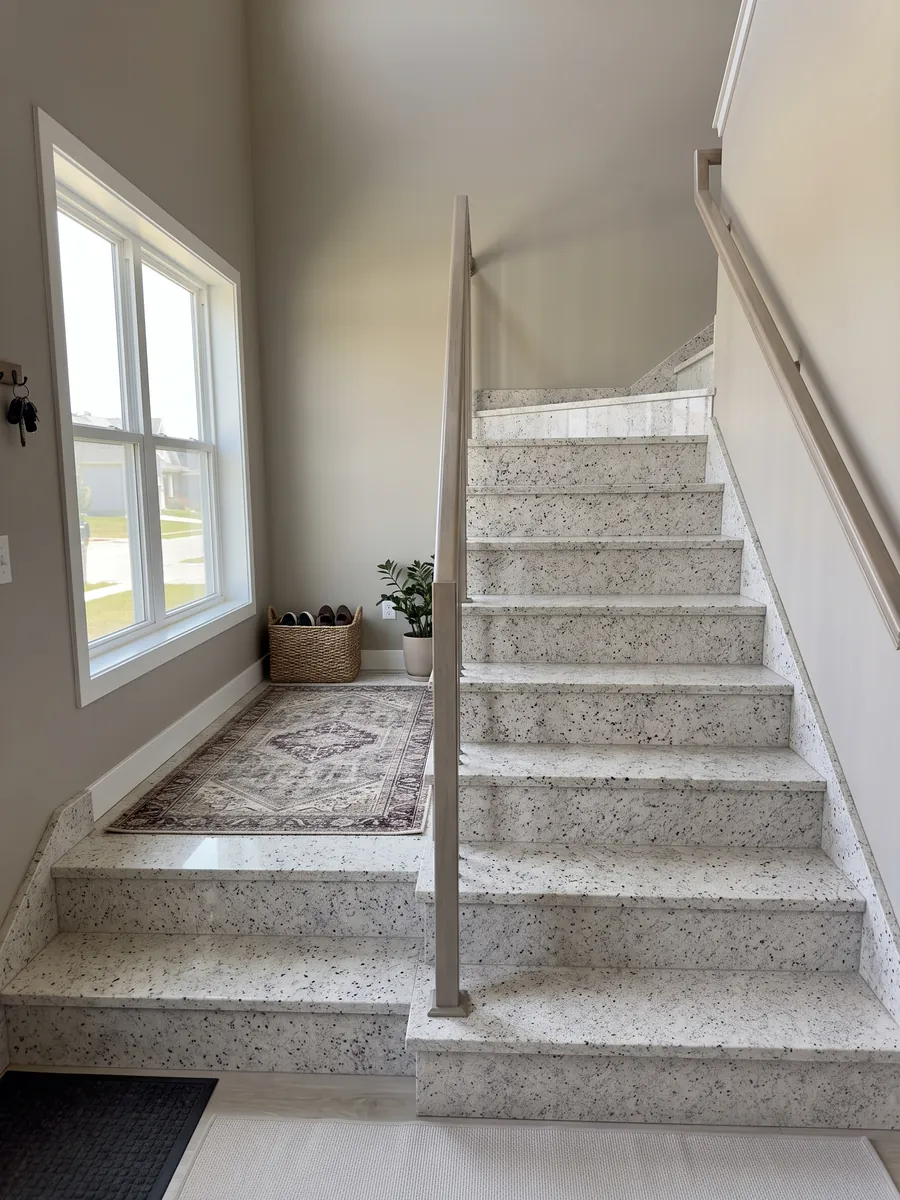 Escalera interior con peldaños de Granito Blanco Dallas con pasamanos: blanco cremoso con un moteado fino gris y pequeños puntos burdeos